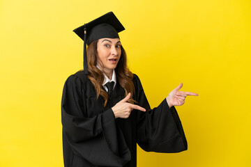 Middle aged university graduate isolated on yellow background surprised and pointing side