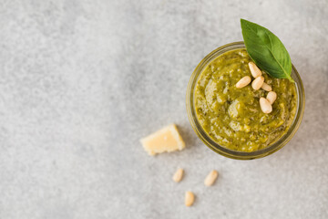 Pesto sauce in a jar with pine nuts, a slice of parmesan and green basil leaves. Top view. Copy space.