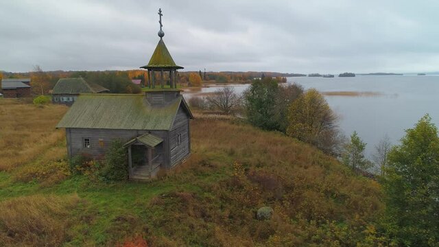 Aerial old small wooden church Chapel St. George Victorious on shore Lake Karelia Russia. Authentic medieval traditional temple. Cloudy rural village. Autumn countryside. Travel landmark film