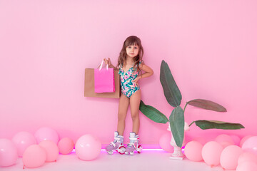 Portrait of a little roller-girl. Shopping, summer, vacation and travel concept. Baby girl in swimwear near pink background.