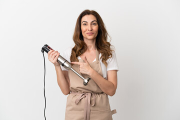 Middle aged caucasian woman using hand blender isolated on white background pointing to the side to present a product