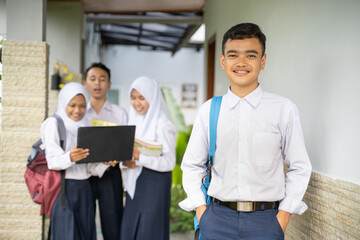an asian teenager smiles at the camera in a school uniform carrying a school bag with copyspace in an outdoor background