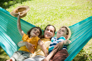 Fototapeta na wymiar mom and Two kids swing in a hammock in a summer park or garden. Concept of friendly family.