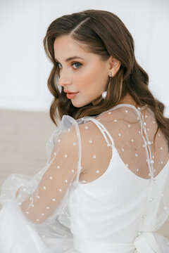 A beautiful young girl with brown hair in a white wedding dress with sleeves. A bride with her hair down in a photo studio. the decor is made of red flowers. the concept of a festive image.