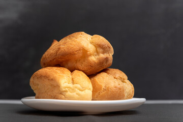 Lush profiteroles on white plate on gray background. Home puffs. Popovers, eclairs. Close up