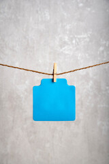 Blank blue paper card hang with clothespin on rope. Copy space. Place for your text. Gray background. Vertical frame