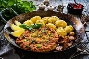 Breaded fried pork chop, potatoes and white mushrooms on wooden table 