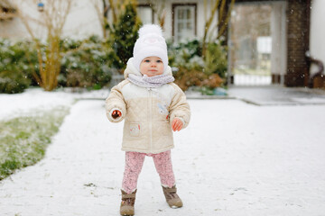 Happy little baby girl making first steps outdoors in winter through snow. Cute toddler learning walking. Child having fun on cold snowy day. Baby's first snow, activity. Winter walk outdoors