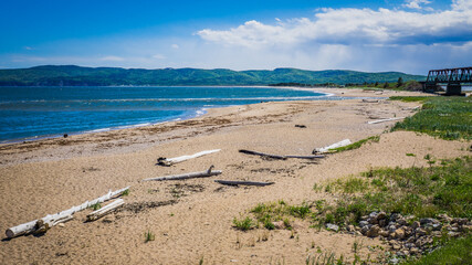 The beach at Barachois (in Gaspesie, Quebec, Canada), with a train railtrack and driftwood on a summer day