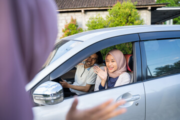 Muslim couple waving from inside the car to a woman wearing a hijab when going home
