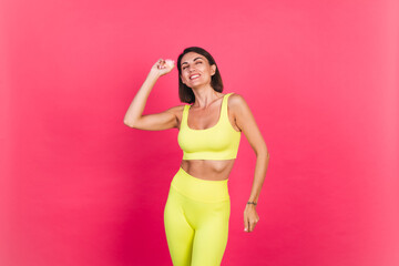 Obraz premium Beautiful fit woman in yellow bright fitting sportswear on pink background happy moving excited perfect body fitness motivation