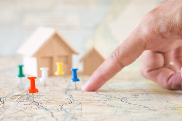 Selective focus of red pin and blurred fingers pointing and house model on map background  for real...