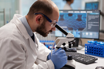 Male scientist looking under microscope at virus sample in medical development laboratory....