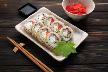 Set of sushi rolls with cream cheese, rice and salmon on a board decorated with ginger on a dark wooden background. Japanese cuisine. Food photo