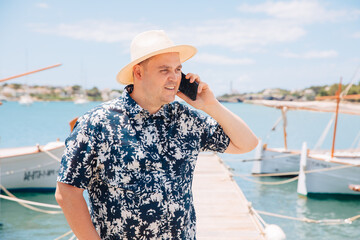 Happy man in straw hat by the sea, speaks on the cell phone . Harbor master is early at the jetty. Enjoy vacation by the sea 