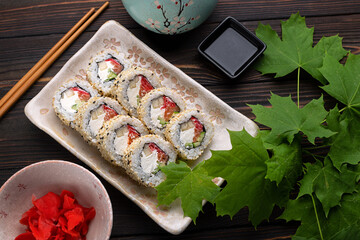 Set of sushi rolls with cream cheese, rice and salmon on a board decorated with ginger on a dark wooden background. Japanese cuisine. Food photo