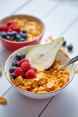 Golden cornflakes with fresh fruits of raspberries, blueberries and pear in ceramic bowl