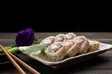 Set of sushi rolls with cream cheese, rice and salmon on a board decorated with ginger on a dark wooden background. Japanese cuisine. Food photo