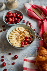 Ceramic bowl of oatmeal porridge with banana, fresh cranberries and walnuts