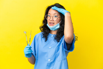 Young asian dentist holding tools over isolated background doing surprise gesture while looking to the side