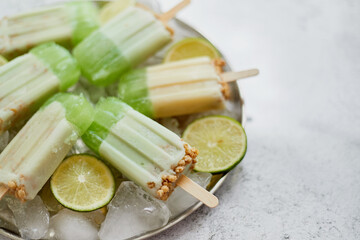 Summer refreshing homemade lime popsicles with chipped ice over stone background