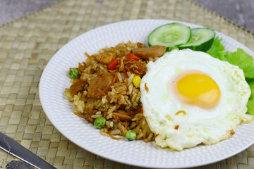 Nasi Goreng or Fried Rice, one of Indonesian popular food, topping with sunny side up egg, cucumber slices, lettuce and crackers. Top view, copy space for text.