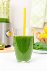 Homemade detox green spinach smoothie with apple and kiwi in glass with drinking straw on kitchen table close-up. Organic vegetables and fruits juice. Healthy eating and slimming diet.