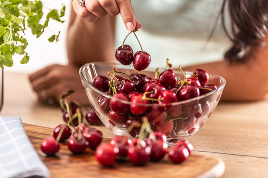 Detail of a glass bowl oif cherries with woman's hand taking couple of them out