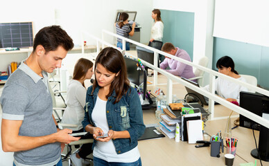 Friendly glad cheerful positive male and female colleagues exchanging phone numbers in modern coworking space