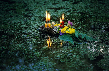 flowers, pentagram amulet and burning candles on dark water background. old national tradition,...