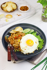 Nasi Goreng or Fried Rice, one of Indonesian popular food, topping with sunny side up egg, cucumber slices, lettuce and crackers. Top view, copy space for text.