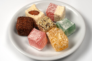 Many pieces of Turkish Delight set on a pile on little white plate. Empty background. Colorful sweet cubes of lokum. Eastern traditional dessert. Copy space.
