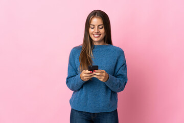 Young Uruguayan woman isolated on pink background sending a message with the mobile