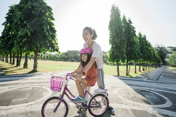 portrait of asian mother Teaching daughter To Ride Bike In the park