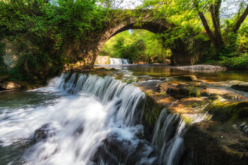 Fototapeta na wymiar water flowing at river with roman bridge at background