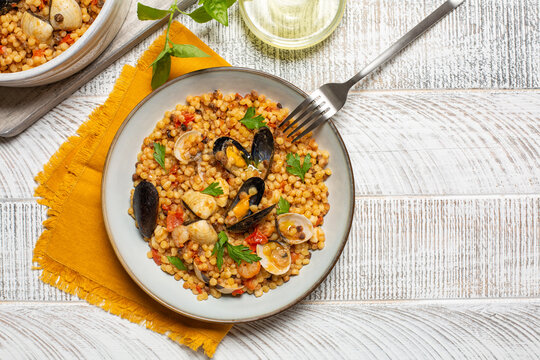 Fregula with seafood, Sardinian pasta consists of semolina dough and toasted in an oven on a white wood background.