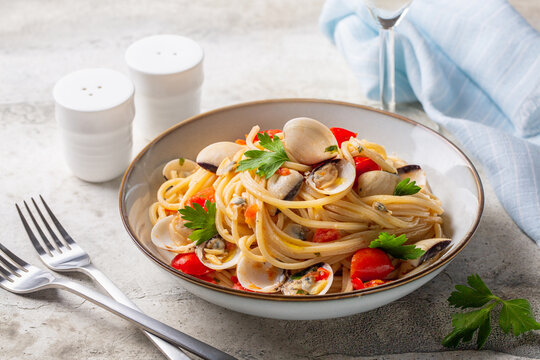 Italian seafood pasta. Spaghetti alle vongole or clams, tomato and parsley. Light stone surface.