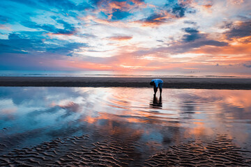 The atmosphere of the beach in the morning, the water on the beach reflects the sky like a mirror. During that time, someone used his hand to touch the surface of the water to ripple.