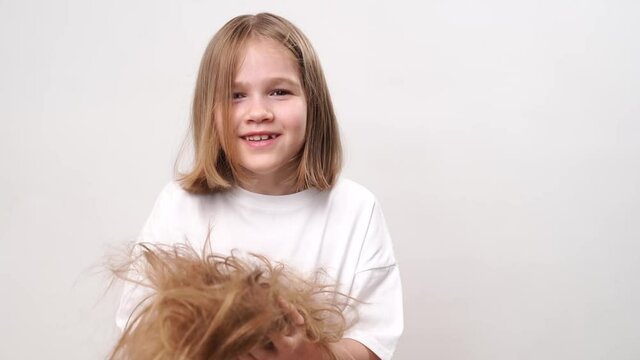 A funny little girl holds in hands cropped hair after cutting and throws them up on a white background. means to care for children's hair. Beauty salon for kids.