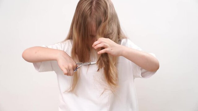 The kid girl shears her long hair with scissors on a white background. Fashionable haircut for the baby. Hairdresser. children's pranks. haircut