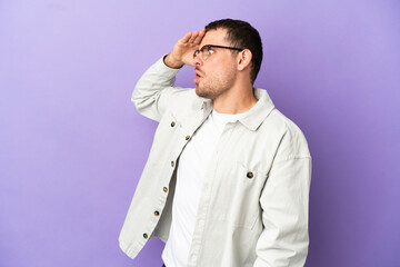 Brazilian man over isolated purple background with surprise expression while looking side