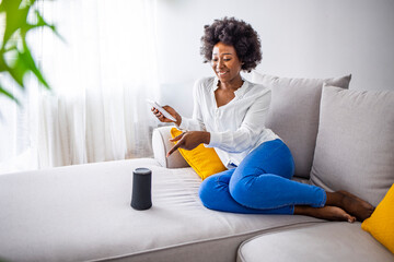 Smart AI speaker concept - Young Woman talk to voice assistant at home and feel happy. Woman talking to smart speaker. Intelligent assistant in smart home system.