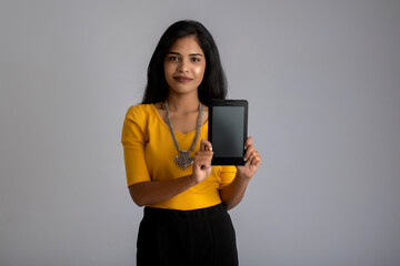 Young beautiful girl holding and showing blank screen of smartphone or mobile or tablet phone on a gray background.