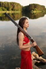 Brunette woman in red bikini with rifle at the lake