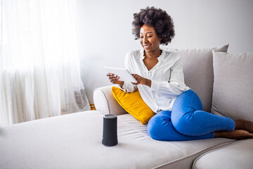 Woman using voice commands to control a smart home devices sitting with a smart speaker and tablet...