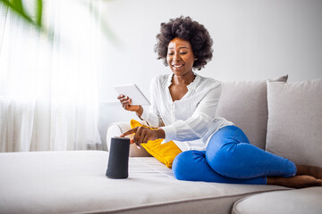 Black woman connecting phone to her virtual assistant smart speaker. Happy black woman using smart...