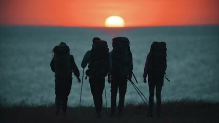 The four travelers walking to the sea shore on sunset background. slow motion