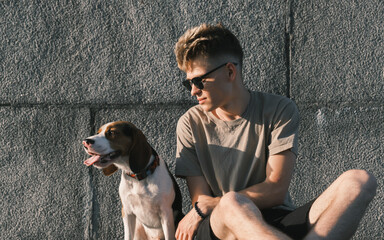 Young man and beagle dog sit together, concrete urban background. Lifestyle with pets, cute puppy...