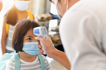Temperature screening and medical checking the student at preschool entrance school. Close-up hand of Teacher with medical infrared thermometer checking the student for Coronavirus prevention.