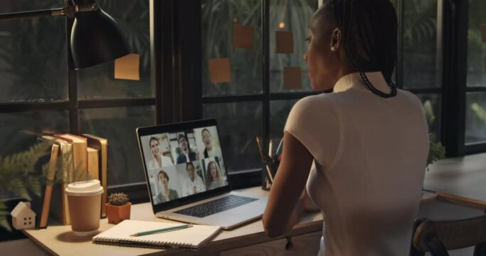 Young African American woman talking with colleagues online via video calling on laptop computer at home during pandemic  
